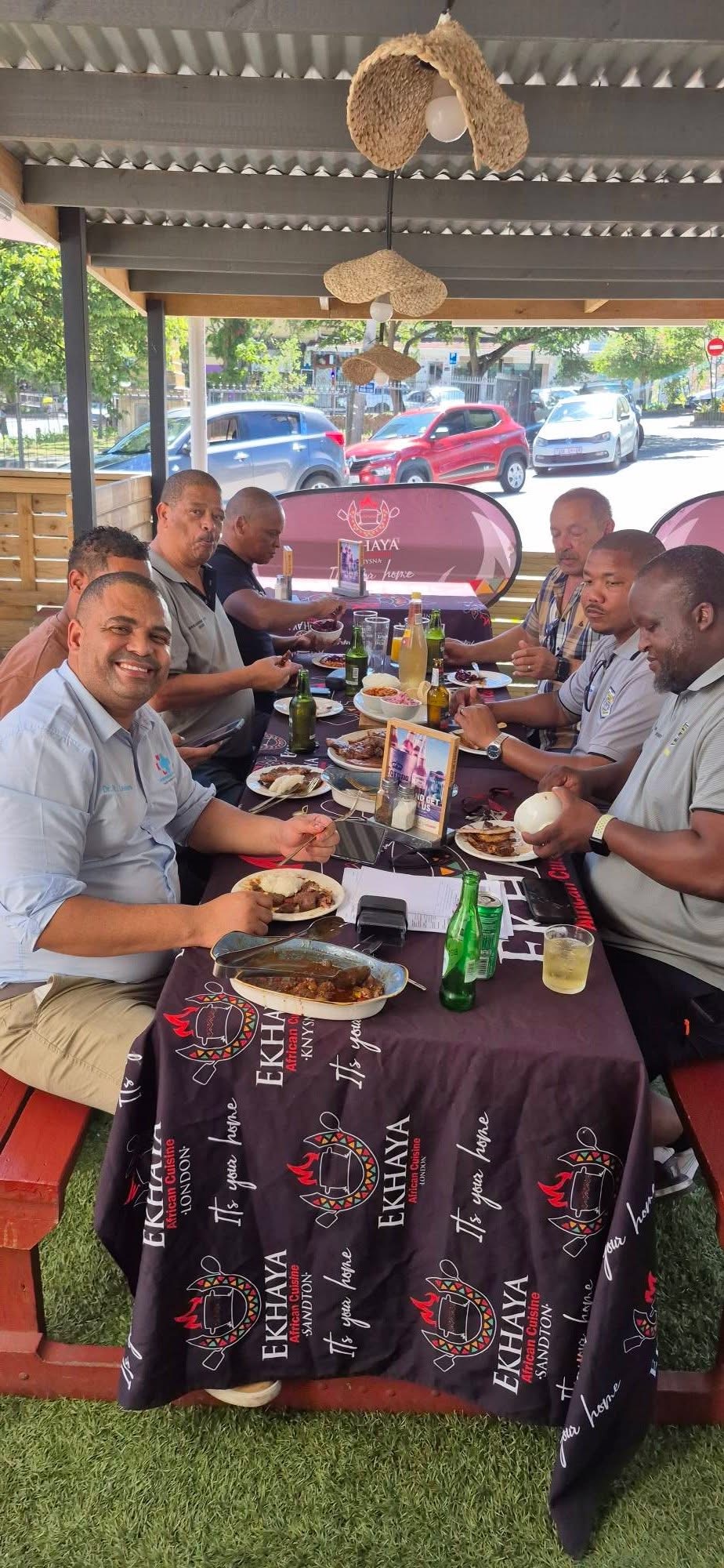 Colleagues sharing a long-table lunch under the Ekhaya awning
